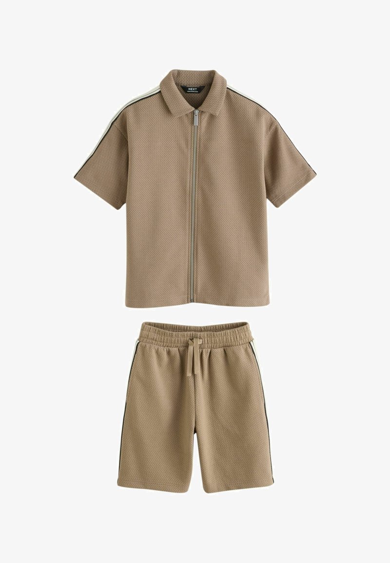 Beige shirt met korte mouwen en rits, met kraag, en bijpassende shorts met elastische taille, beide voorzien van zwarte en witte strepen aan de zijkant.