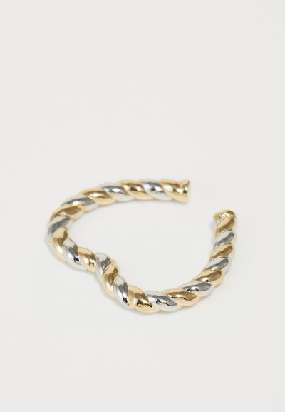 Sukryžiuota metalo apyrankė su pakaitiniais auksiniais ir sidabriniais paviršiais, išryškinanti lygią, blizgią tekstūrą ir suapvalintais galais.