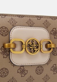 Hnědá kabelka s vzorem a zlatým kovovým detailem uprostřed. Hladký béžový kožený detail s kulatým logem a prošitím.