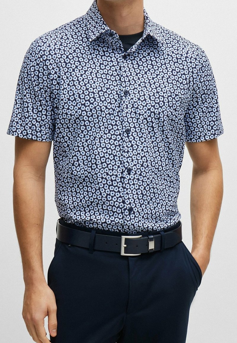 Košile s krátkým rukávem v námořnické modré barvě s bílým květinovým vzorem. Vyrobena z hladkého materiálu, má klasický límec a rovný střih.