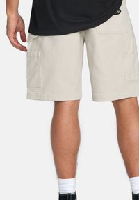 Beige cargo shorts i slidstærkt stof, med to sidelommer og en afslappet pasform. Længden når midt på låret, parret med en sort top og sko.