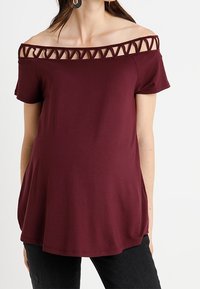 Burgundy off-shoulder topp med snördetalj längs halsringningen. Korta ärmar, mjukt tyg och en flödande, avslappnad passform.