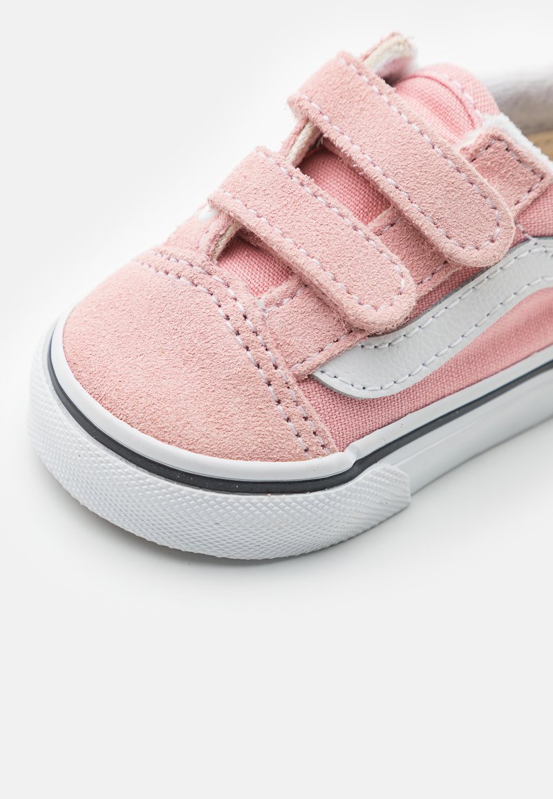 Roze suède sneaker met witte canvas accenten, voorzien van twee klittenbandsluitingen, een gestructureerde rubberen zool en een zwarte rand rondom de zool.
