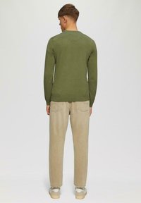 Grünes Longsleeve-Shirt mit Rundhalsausschnitt, strukturiertem Stoff und lockerer Passform, kombiniert mit hellbeigen Hosen und Sneakers mit niedrigerem Schnitt.