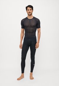 Schwarzes sportliches Oberteil mit kurzen Ärmeln und Netzdetails, kombiniert mit schwarzen, enganliegenden Leggings; beide aus glattem, dehnbarem Stoff gefertigt.