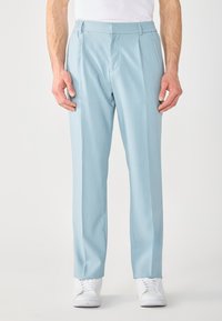 Pantaloni azzurri chiari con un taglio su misura, cintura elastica, tasche laterali e una texture liscia. Abbinati a sneakers bianche.
