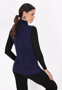 Marineblaue weiche Fleece-Weste mit hohem Kragen, ärmellosem Design und glatter Textur, kombiniert mit einem schwarzen Langarmshirt und Leggings.