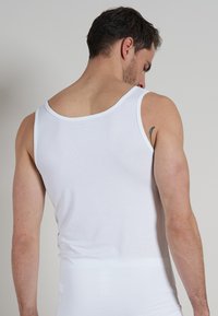 Weißes Baumwoll-Top mit breiten Schulterträgern und einer taillierten Passform. Glatte Textur, minimalistischer Stil, keine sichtbaren Muster oder Verzierungen.