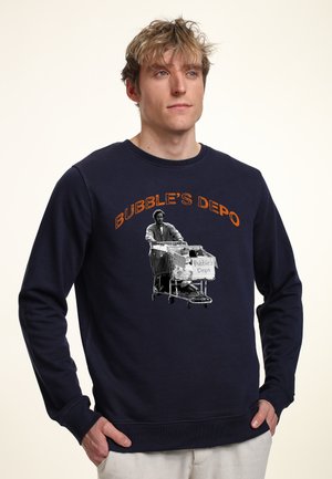 Mørkeblå sweatshirt med et grafisk motiv af en person med indkøbsvogne, tekst "BUBBLE’S DEPO" i orange, rund hals, ribbede manchetter.