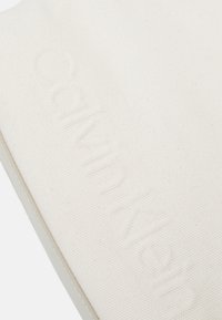 Witte katoenen canvas tas met reliëf logo van Calvin Klein. Soepele textuur, minimalistisch ontwerp, vierkante vorm en een contrasterende lichtgrijze rand.