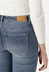 Lieknos mėlynos džinsinės kelnės su šviesiu plaunimu, su užpakalinėmis kišenėmis ir tan odiniu ženklu su tekstu "Vero Moda We Do Denim".
