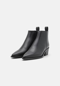 Botas de âncles de pele preta com bico pontiagudo, salto bloco, textura suave e laços na parte traseira para facilitar o calçar.