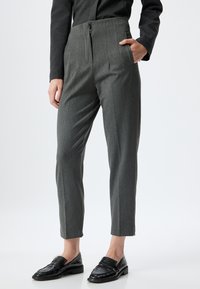 Grijze op maat gemaakte broek met zijzakken, een ritsluiting en een taps toelopend ontwerp. Draagt met zwarte loafers met een textuurpatroon.