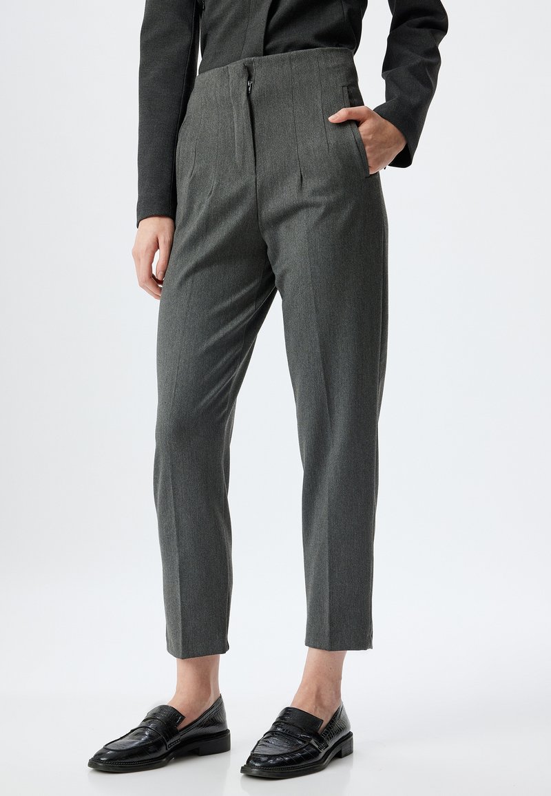Grijze op maat gemaakte broek met zijzakken, een ritsluiting en een taps toelopend ontwerp. Draagt met zwarte loafers met een textuurpatroon.