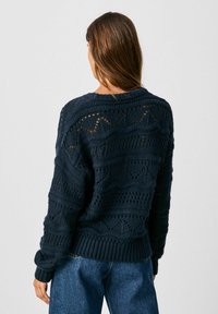 Donkerblauwe gebreide trui met een gestructureerd patroon en opengewerkt ontwerp, voorzien van een geribbelde zoom en manchetten, gezien vanaf de achterkant.