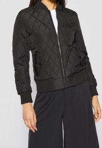 Giubbotto bomber trapuntato nero con zip frontale, polsini a coste e due tasche laterali. Materiale leggero con finitura testurizzata.