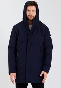 Parka à capuche bleu marine avec fermeture éclair à l'avant, bouton-pression et poches latérales ; fabriquée dans un matériau lisse et résistant à l'eau.