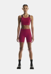 Fitted athletic set in bright pink, featuring a cropped sports bra with black straps and mid-rise shorts, smooth texture, and minimal design.