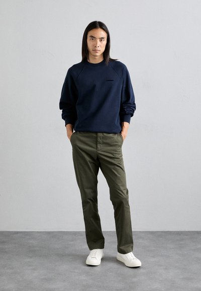 Sudadera azul marino con mangas raglán, pantalones verdes oliva y zapatillas blancas. Diseño minimalista con un pequeño logo en el pecho.