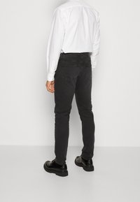 Vaqueros de mezclilla negros con un corte ajustado, que cuentan con bolsillos traseros y una cintura de altura media, combinados con zapatos de cuero negros y una camisa blanca.