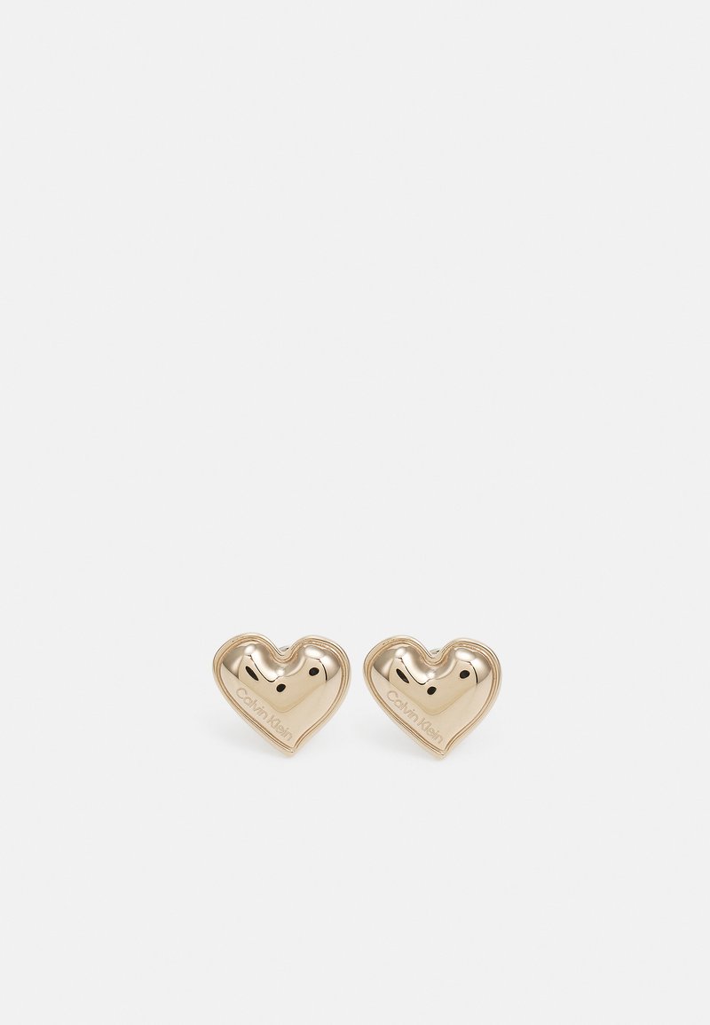 Pendientes en forma de corazón de tono dorado con textura suave, que presentan suaves curvas y un detalle de marca, diseñados para un aspecto contemporáneo.