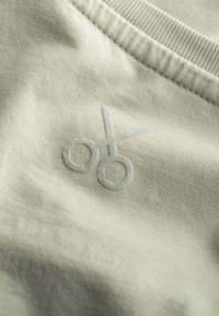 Light beige fabric featuring a textured surface with an embroidered scissor motif in a slightly darker shade.