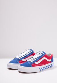 Červené a modré tenisky s bílými tkaničkami, svršek z semiše, bílé akcenty po stranách a kostkovaný vzor na podrážce. Design s kulatou špičkou.