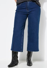 Modré džínové culottes s třásněmi na lemu. Obsahují pět kapes a poutka na opasek. Kombinované s černými koženými botami se cvočky pro kontrast.