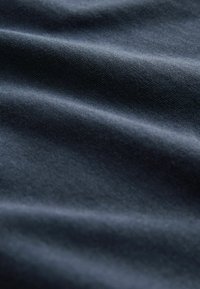 Donker marineblauwe stof met een gladde, licht glanzende textuur, met subtiele lichtreflecties en zachte rimpelingen in het materiaal.