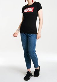 Camiseta de algodón negra con un atrevido logo rojo de "MARVEL", combinada con jeans azules y zapatillas deportivas negras. Diseño minimalista con una forma ajustada.