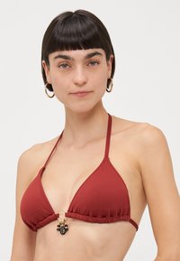 Red triangular bikini top with a gold ring and decorative embellishments at the center. Made of smooth fabric with adjustable straps.