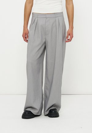 Person wearing light gray wide-leg pleated trousers and black chunky shoes, standing against a plain white background.