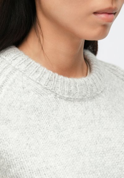 Svetlosivý sveter s rebrovaným okrúhlym výstrihom. Pletená textúra s jemným povrchom. Záber zblízka na oblasť ramena a krku.