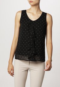 Top sin mangas negro con lunares blancos, que presenta un detalle de volantes verticales en la parte delantera y un dobladillo inferior transparente.