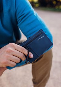 Navy blue wallet with a smooth texture, featuring a zip compartment, card slot, and a keychain loop. Minimalist design with logo detail.