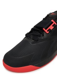 Czarny but sportowy z teksturowaną cholewką, czerwoną podeszwą i czerwonym zapięciem na klamrę. Posiada siatkowe akcenty i warstwowy design dla wsparcia i przyczepności.