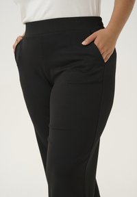 Pantalons noirs extensibles avec une texture lisse, dotés de poches latérales et d'une taille élastique, conçus pour le confort et la flexibilité.