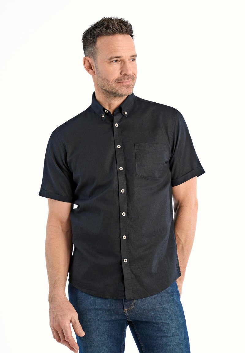 Camicia nera a maniche corte con bottoni, realizzata in tessuto testurizzato, con taschino sul petto e bottoni bianchi, abbinata a jeans in denim blu.