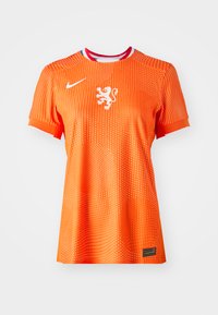 Orange Nike fotbollströja med korta ärmar, prydd med en vit lejonemblem, prickig struktur och en krage med röd och blå accent.