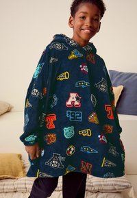 Marineblå fleece-poncho med hætte, der har forskellige farverige lapper, logoer og tal. Overdimensioneret design med lange ærmer og en kengurulomme.