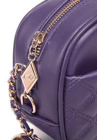 Borsa a tracolla in pelle viola con design trapuntato, zip e accessori in tonalità oro. Include una tracolla a catena e un ciondolo decorativo.