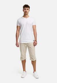 T-shirt blanc à col en V, shorts cargo beiges à ourlets roulés et sneakers blancs. Look décontracté, texture lisse et détails de design minimalistes.