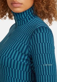 Golf o wysokim kołnierzu wykonany z miękkiego materiału w ciemnoniebieskie i turkusowe paski, z detalem w postaci zamka oraz logo na ramieniu.