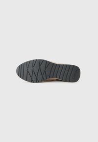 Semelle d'une chaussure beige avec une bande de roulement en caoutchouc noir présentant des rainures diagonales et le nom de la marque « Gabor » embossé près du talon.