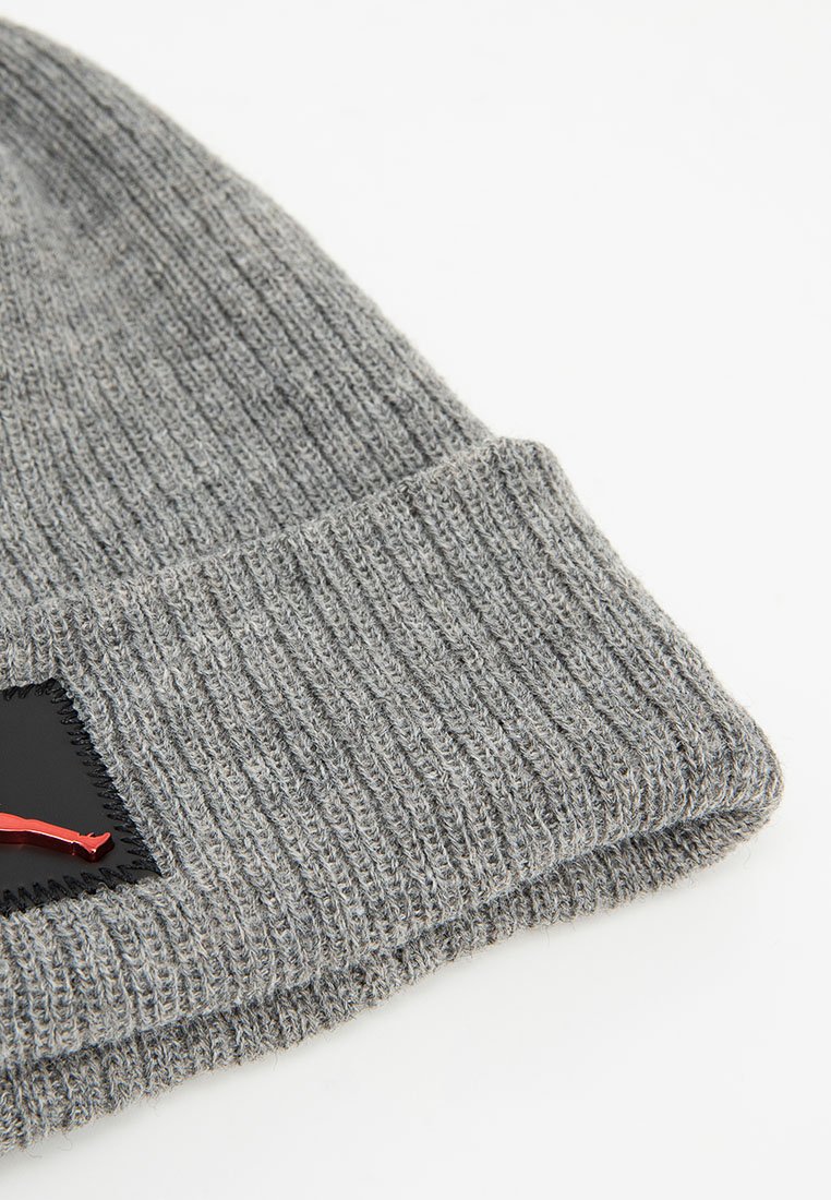 Graue gerippte Strickmütze mit umgeschlagenem Bund, die ein kleines schwarzes Patch mit rotem Design auf weißem Hintergrund zeigt.