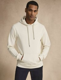 Off-white hoodie med snörning, känguruficka, ribbade ärmslut och nederkant, tillverkad av mjukt tyg. Bärs med mörka byxor.