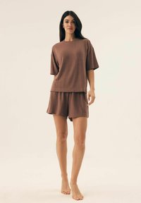Brązowy zestaw do lounge z prążkowanym wzorem, składający się z koszulki z krótkim rękawem i szortów z wysokim stanem. Miękka tekstura, luźny krój i skromna długość.