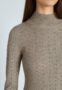 Maglione beige a collo alto a coste con paillettes decorative. Design aderente, lavorazione a maglia testurizzata e maniche lunghe. Tessuto morbido e lucentezza sottile.