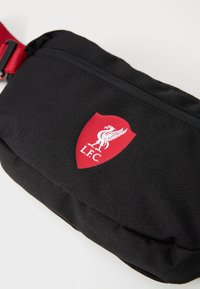 Sort stofslinget med en glat overflade, prydet med et rødt Liverpool FC-skjold logo på fronten og en justerbar rød rem.
