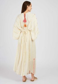 Langer, cremefarbener Kaftan mit goldenen Streifen, rosa und orangefarbigen Quasten auf der Rückseite und floralen Akzenten an den Seiten. Leichter Stoff, lockere Passform.